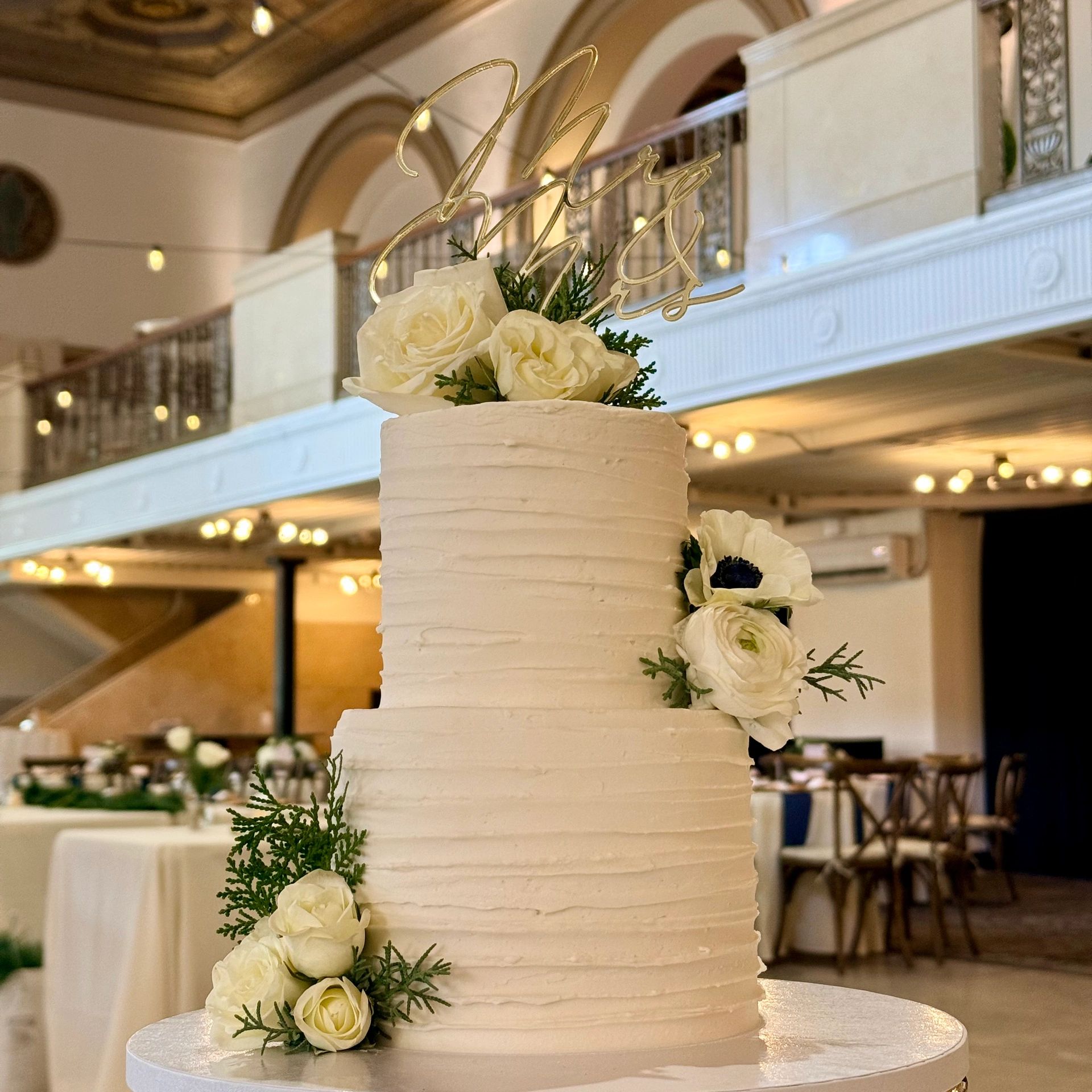 Elegant white wedding cake adorned with fresh flowers and a gold topper.