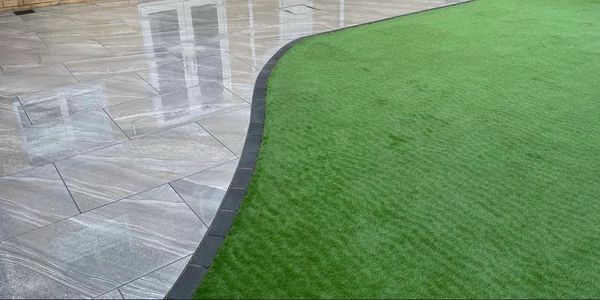Wet tiled patio next to a lush green lawn with a curved border.