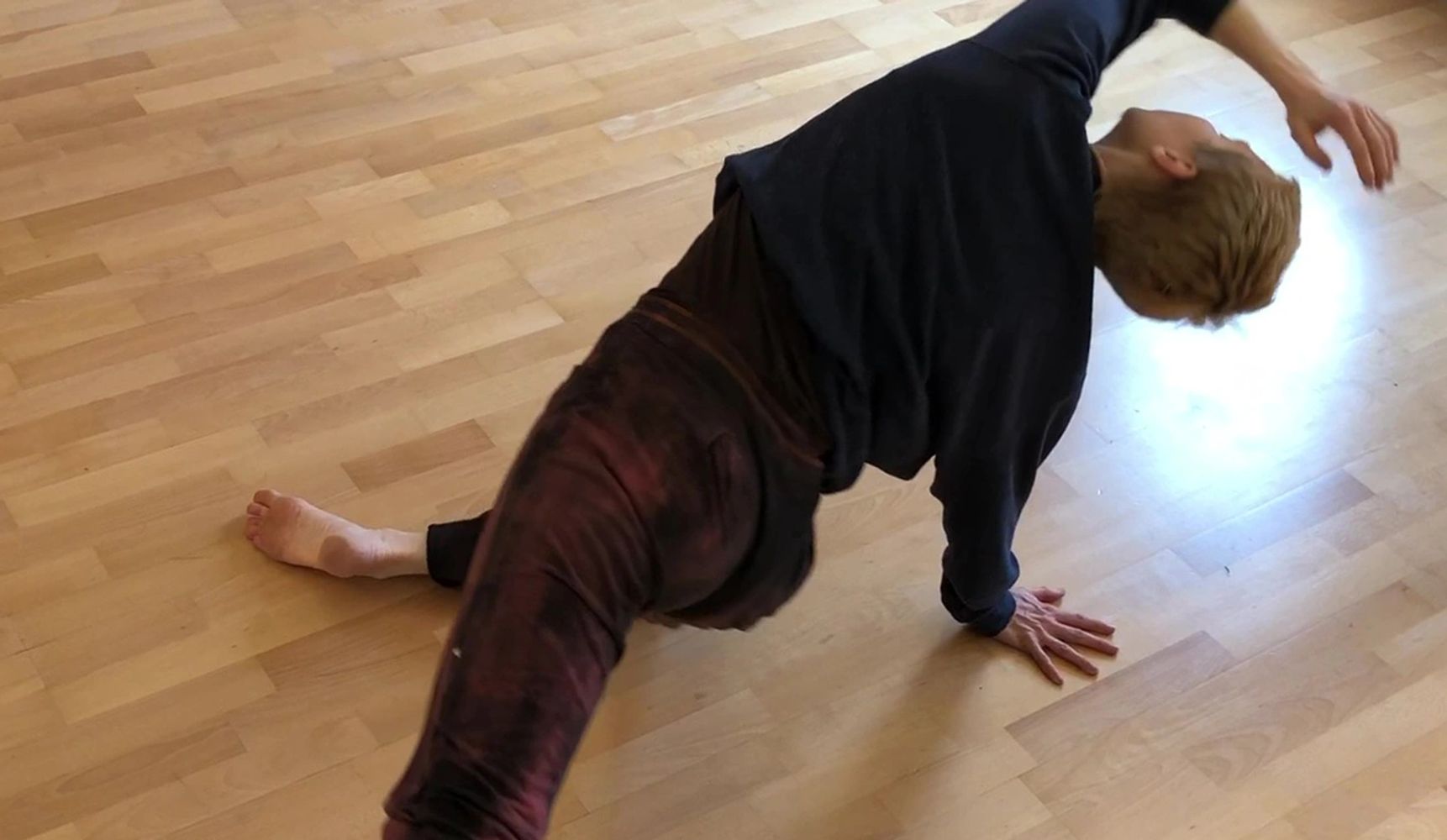 Kathleen Rea lunges on a light wood floor   with one arm reaching upwards.