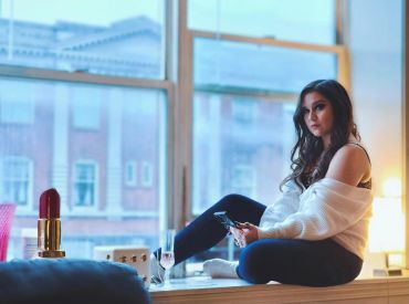 Woman sitting by a window, holding a glass of wine, looking contemplative.