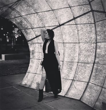 Woman in a black dress posing under a curved, illuminated structure at night.