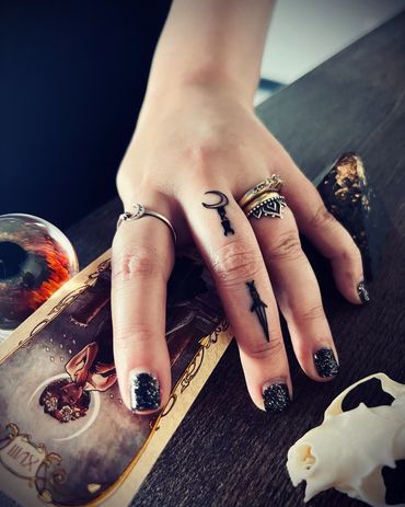 Hand adorned with rings and black glittery nail polish resting on a mystical card.