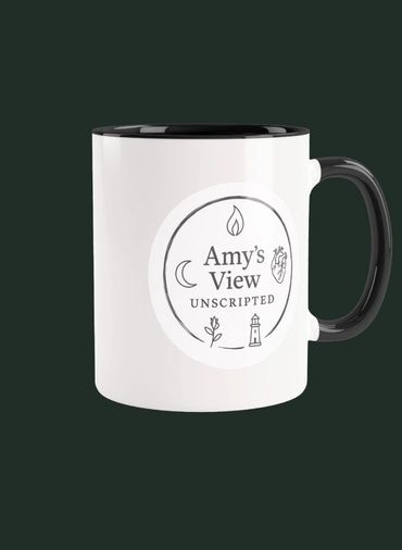 White mug with black handle and rim, featuring a circular logo for 'Amy's View UNSCRIPTED'.