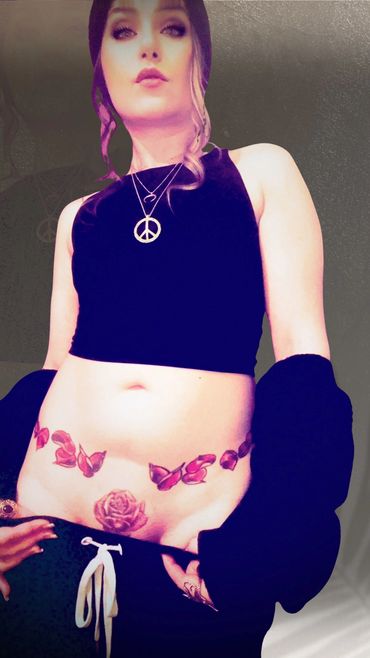 Woman with butterfly and rose tattoos, wearing a black crop top and peace necklace.
