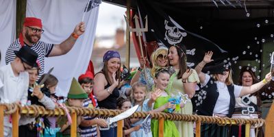 A lively pirate-themed parade with children and adults in costumes waving happily.