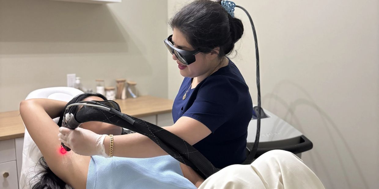 Woman receiving laser hair removal treatment on her underarm in a clinic.