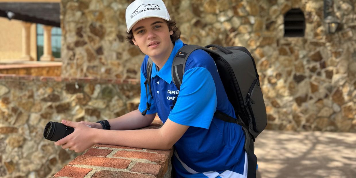 Young photographer in blue shirt and white cap holding a camera lens outdoors.