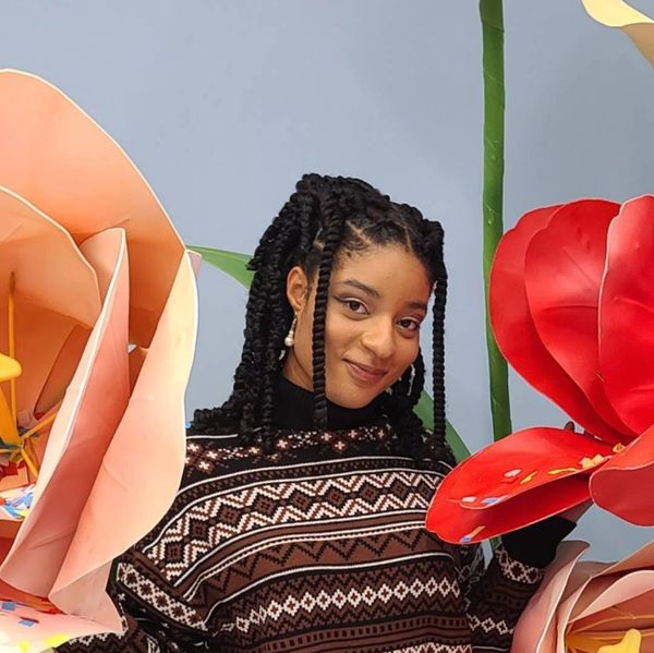 Young woman with braided hair posing among large colorful paper flowers.