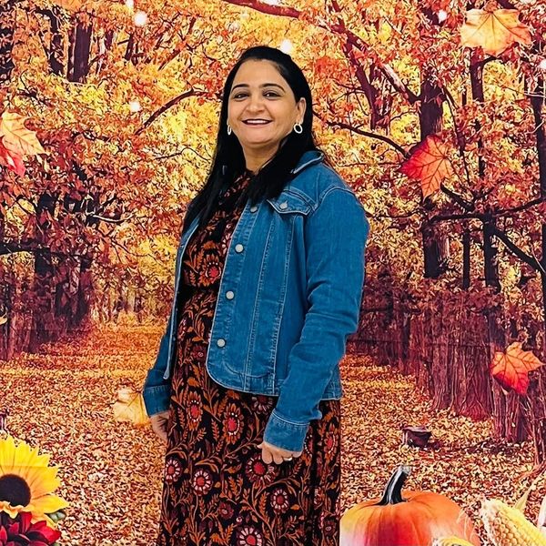 Woman smiling in autumn-themed setting with pumpkins and colorful leaves.