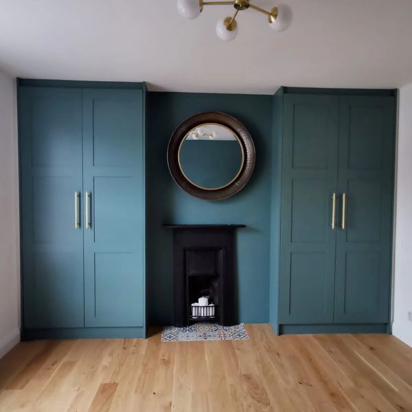 Minimalist room with teal cabinets, a small black fireplace, and a round mirror above it.