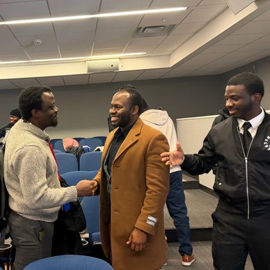 Three men engaging in a friendly handshake and conversation in a meeting room.