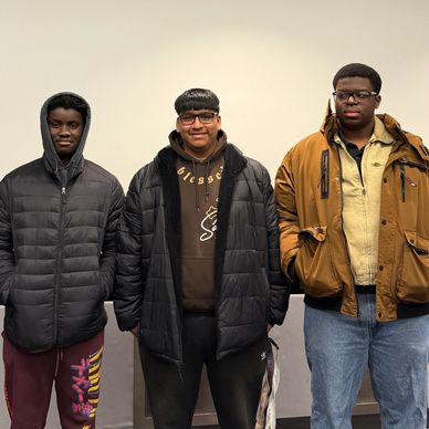 Three young men wearing jackets stand side by side against a plain background.