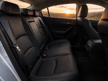 Interior view of a car's backseat with black leather seats and a sunset outside.