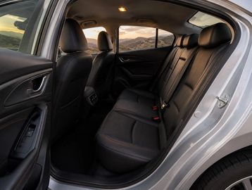 Rear interior of a modern car with black leather seats and open door.