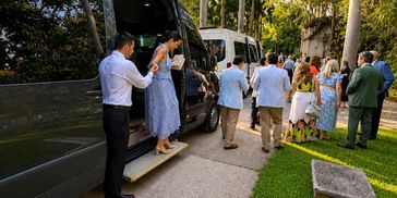 A man helps a woman step out of a van during a gathering.