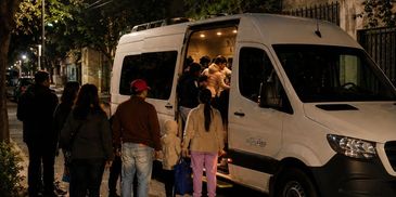 People boarding a white van at night on a city street.