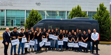 A group of people in black shirts posing with certificates in front of a van.