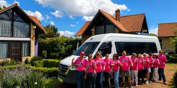Grupo de personas con camisetas rosas delante de una furgoneta blanca.
