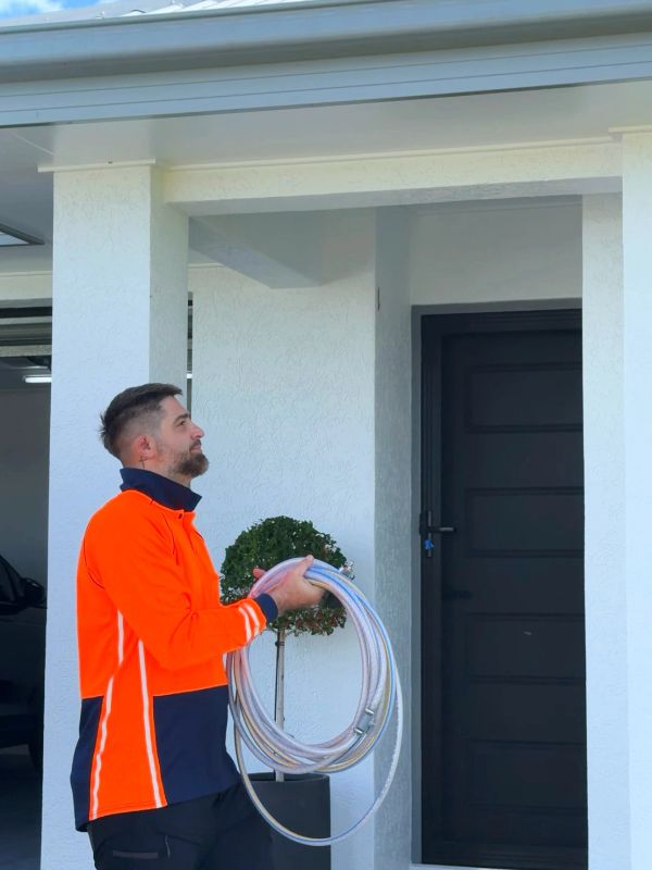 Man in safety jacket holding coiled hose outside a house.