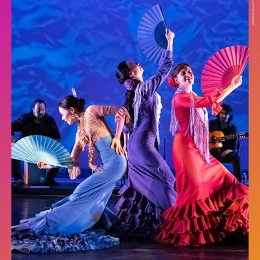 Three women performing flamenco with colorful fans and dresses.