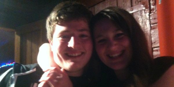 Two people smiling closely together in a dimly lit setting.