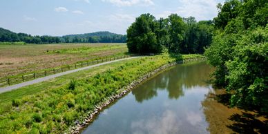 A calm river beside a pathway with trees.