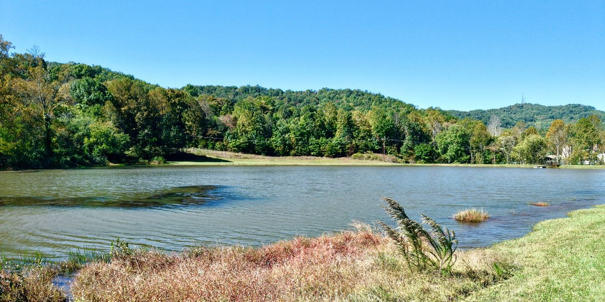 Peaceful lake surrounded by green hills and blue sky.