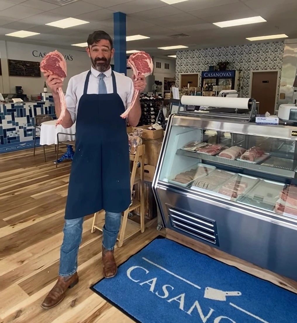 Butcher proudly holding two large steaks inside Casanova's butcher shop.