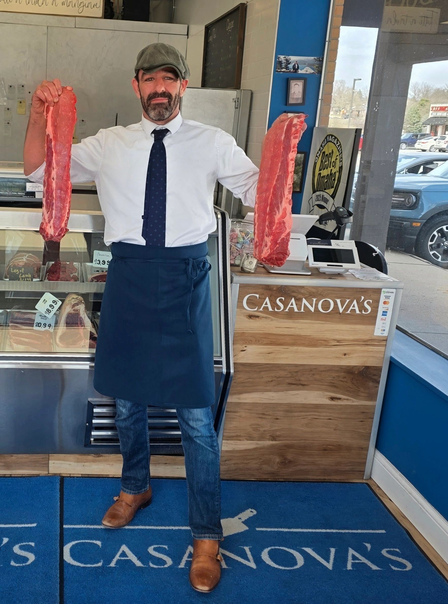 Man holding two large cuts of raw meat in a butcher shop.