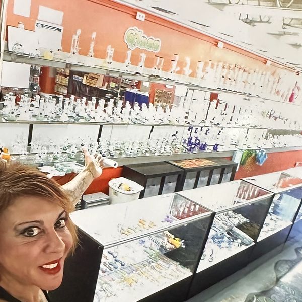 Woman pointing inside a glass shop filled with glass pipes and bongs.