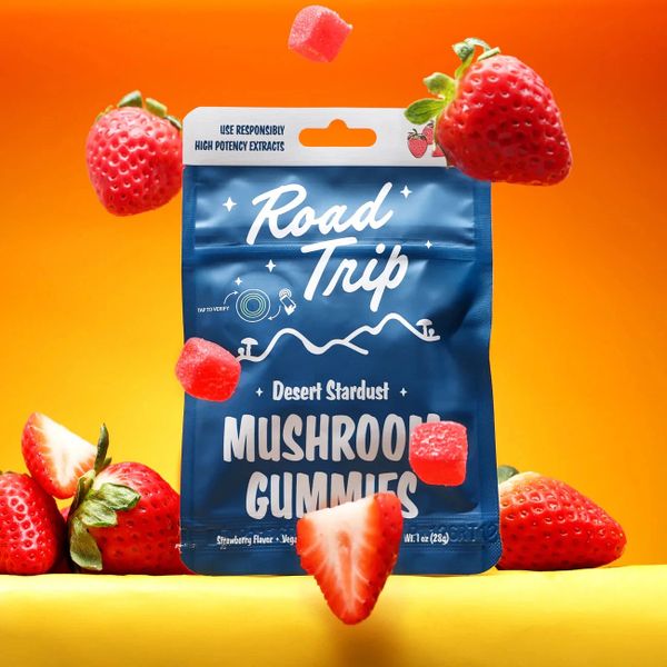 Blue bag of Road Trip Desert Stardust Mushroom Gummies surrounded by strawberries.