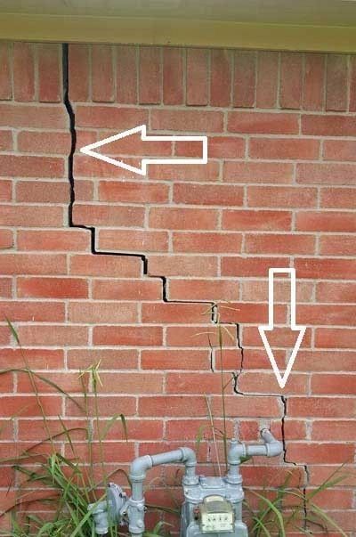 Large crack in a brick wall with white arrows pointing at it.