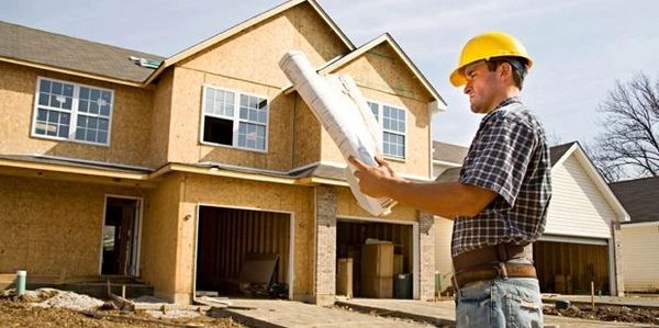 Construction worker reviewing blueprints outside a house under construction.