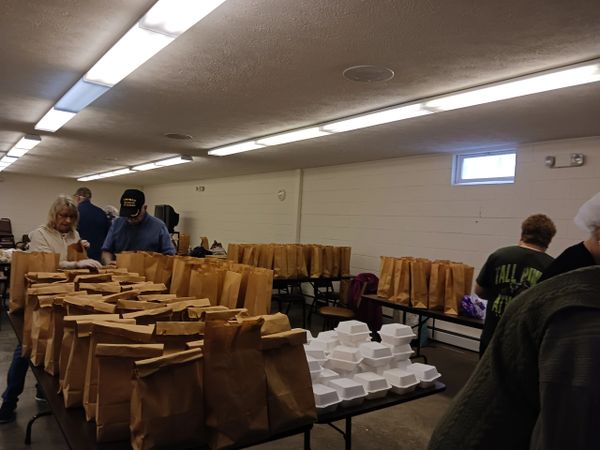 People packing brown paper bags and white food containers in a large room.