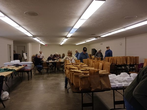 Volunteers packing meals in brown bags and white containers in a community hall.