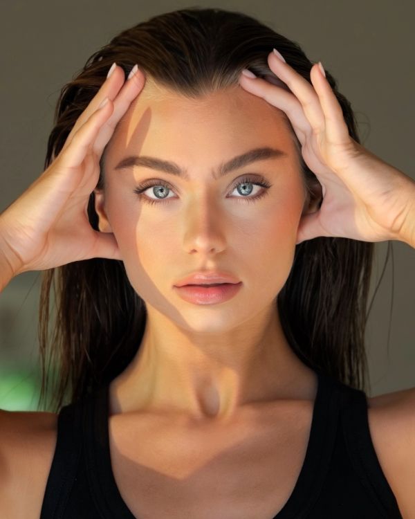 Woman with striking blue eyes holding her head.