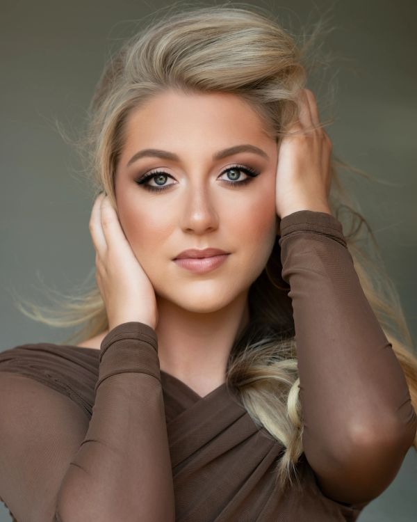 Portrait of a blonde woman with striking makeup and a brown top.