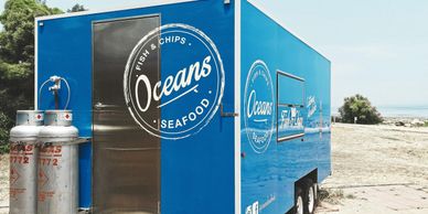 Blue seafood food truck named Oceans parked on a sandy beach.