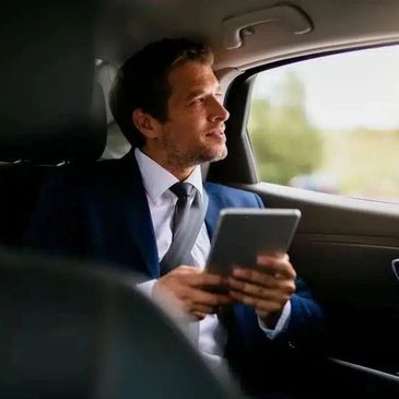 Businessman in a suit looking out car window holding a tablet.
