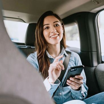 Smiling woman using smartphone in a car backseat.