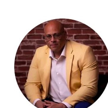 Man in yellow blazer sitting against brick wall.