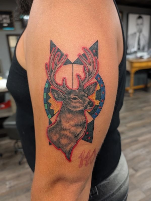 Tattoo of a deer with antlers surrounded by colorful geometric shapes on an arm.