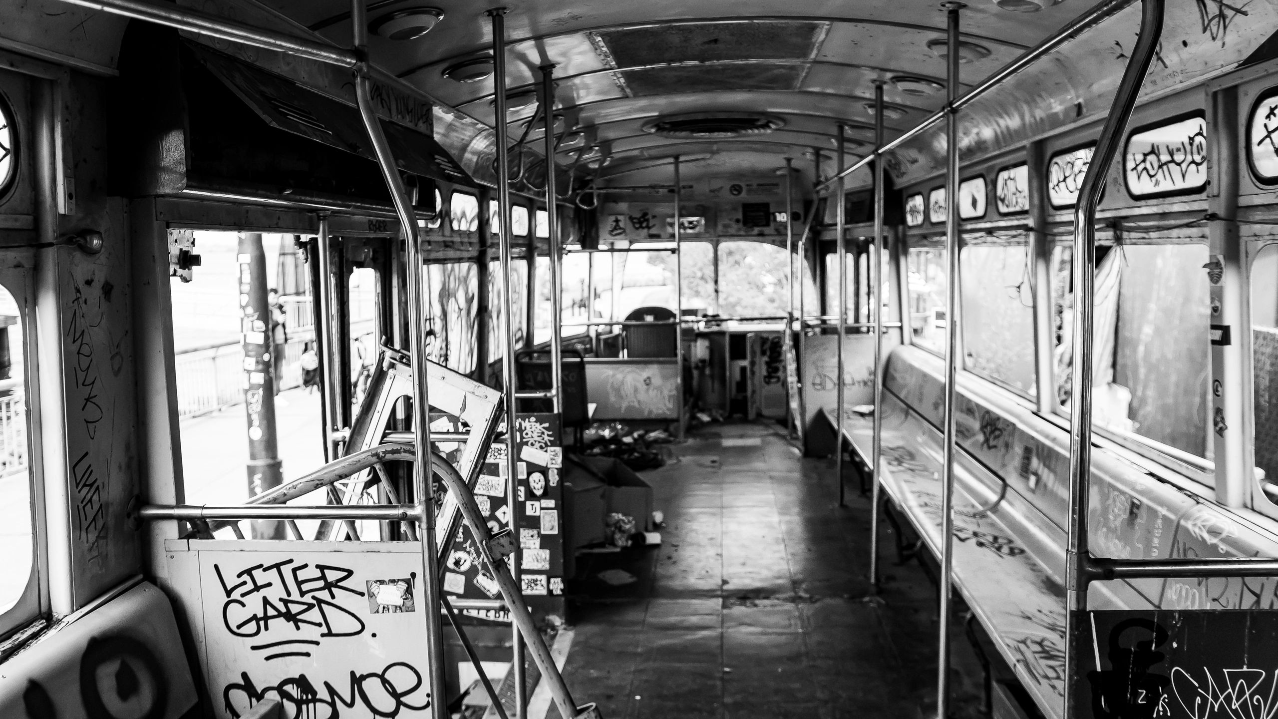 Interior of an abandoned, graffiti-covered bus in black and white.
