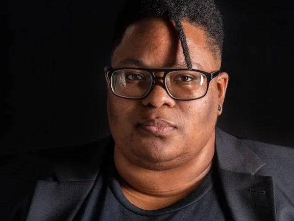 A photo of a transmasculine person in a black jacket staring intently at the camera. 