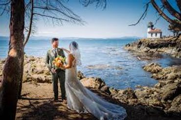 Bride and groom by rocky seaside with lighthouse in background.