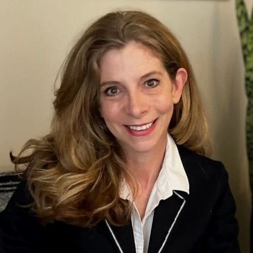 Smiling woman with long wavy hair in a black blazer and white shirt.