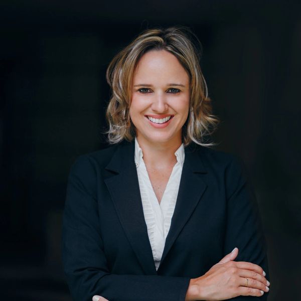 Professional woman smiling confidently in business attire against dark background.