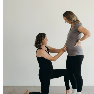 Two women interacting, one kneeling and touching the other's pregnant belly.