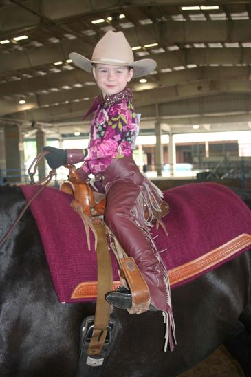 Young child in cowboy attire riding a horse indoors.