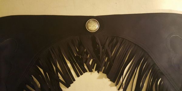 Close-up of a dark fringed leather item with a decorative button.
